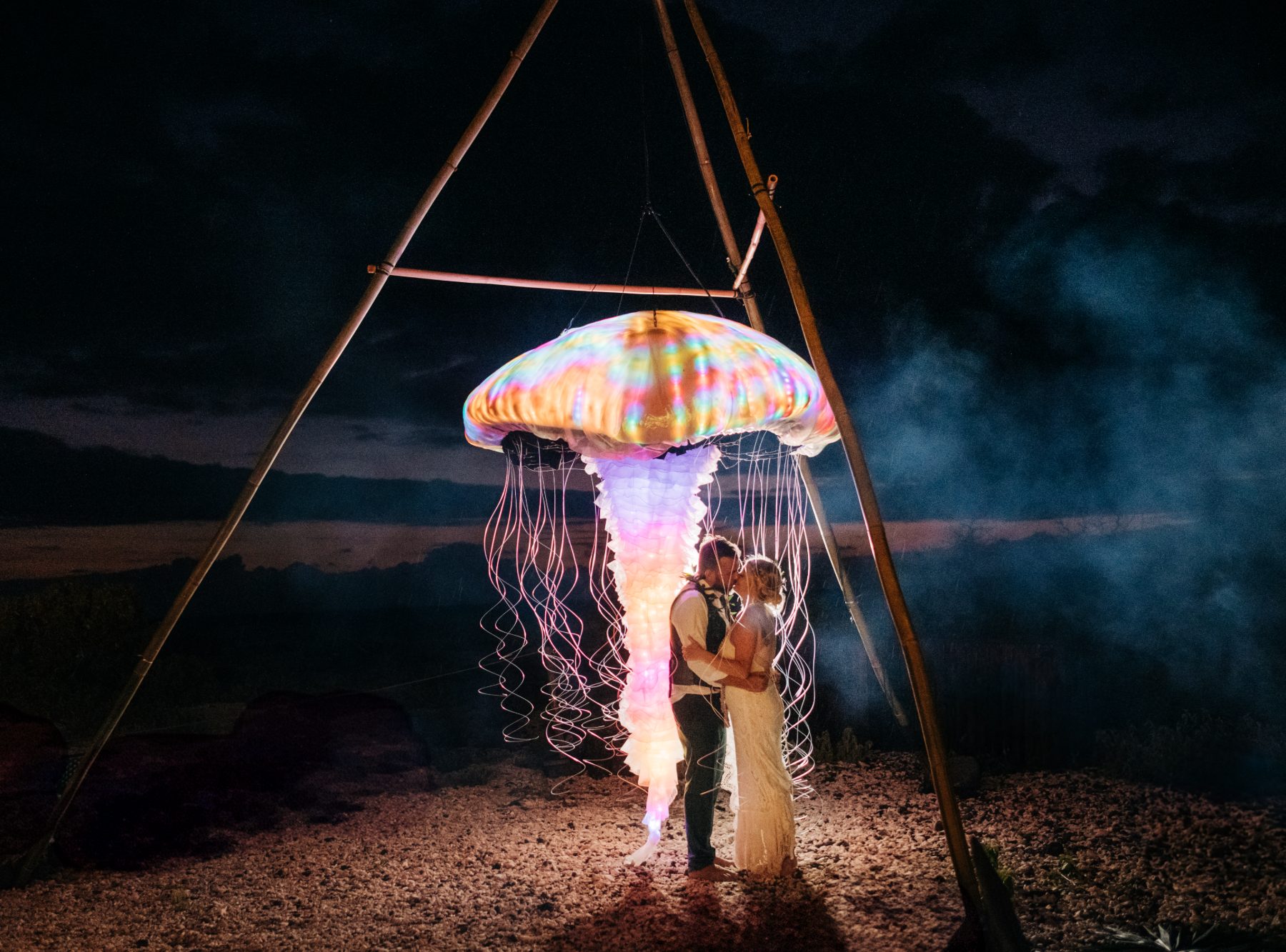 Newlyweds kissing under the suspended LED jellyfish sculpture at a Big Island wedding reception