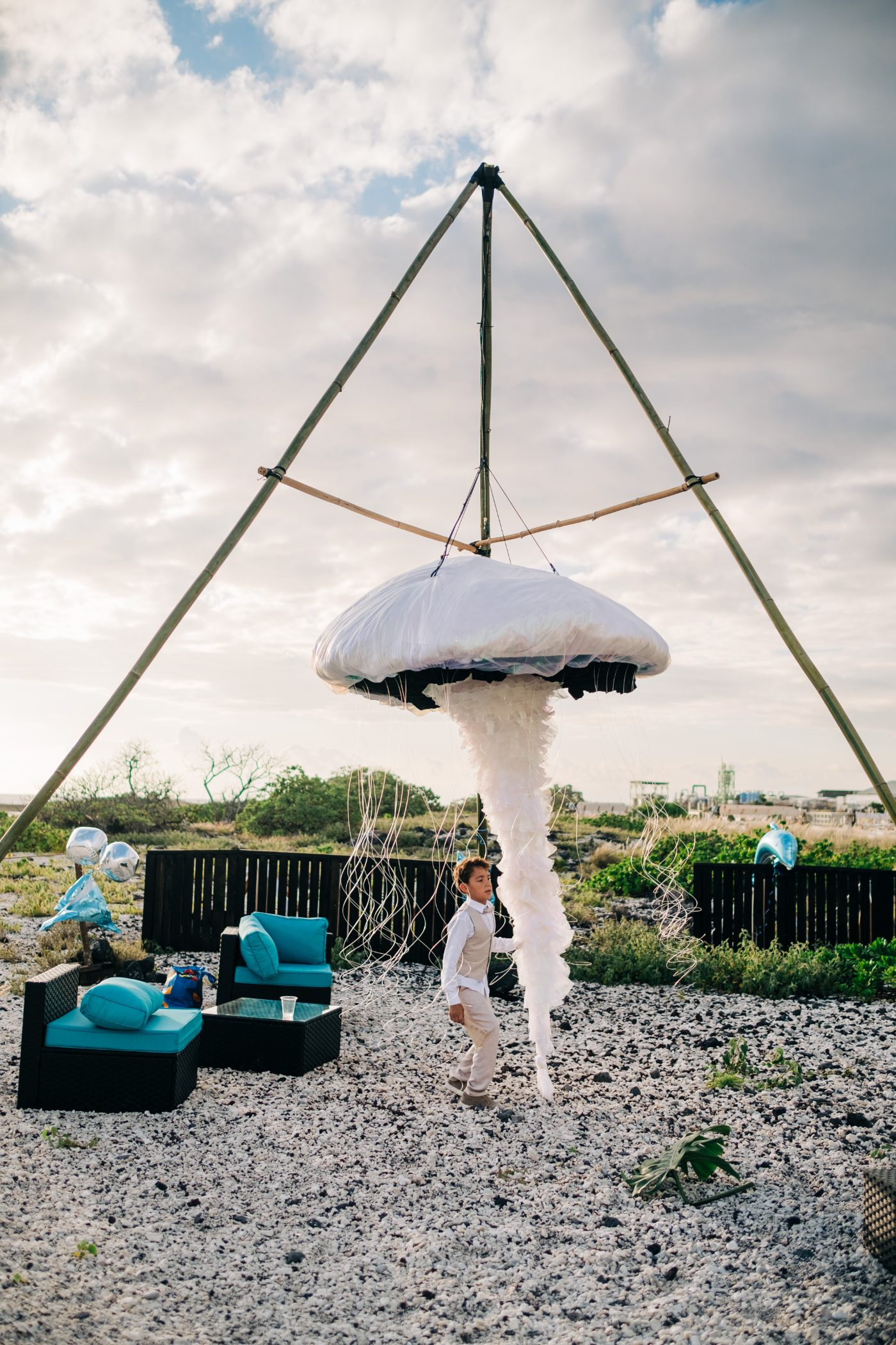 LED jellyfish sculpture rigged on a bamboo tripod above a lounge setup in daylight at Kona Salt Farm