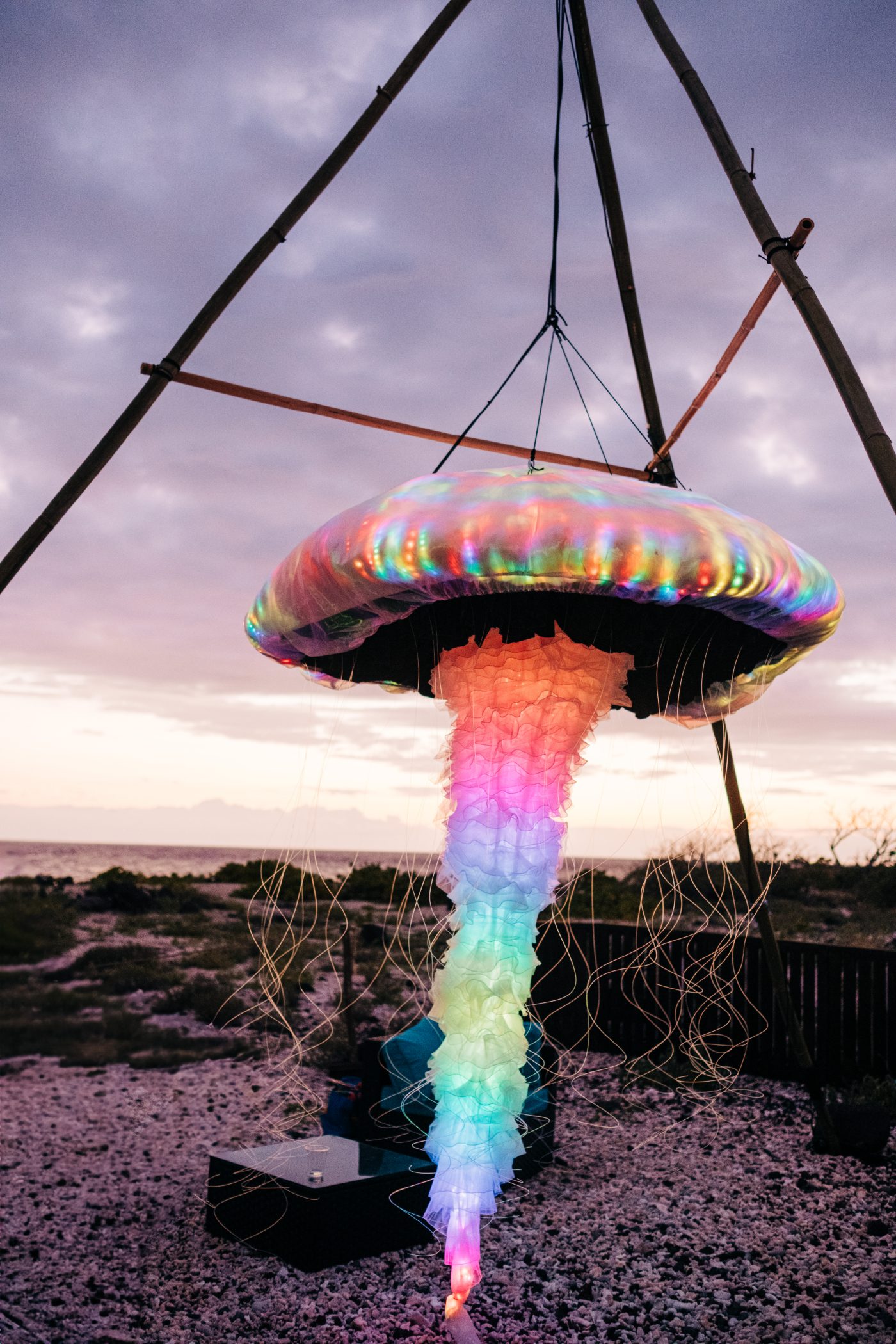 LED jellyfish sculpture glowing full rainbow over an oceanfront Big Island event at dusk